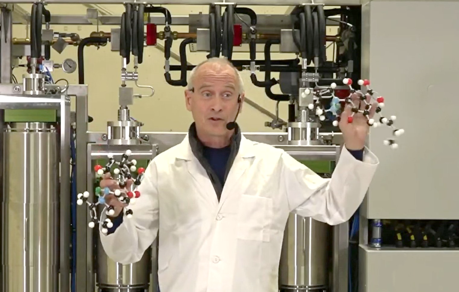 A man in lab coat standing next to pipes.